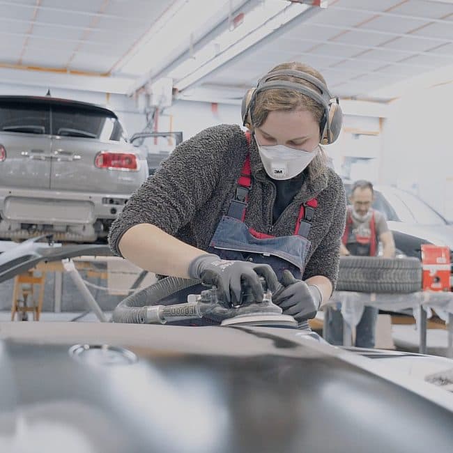Jeune en formation ponçant une carrosserie